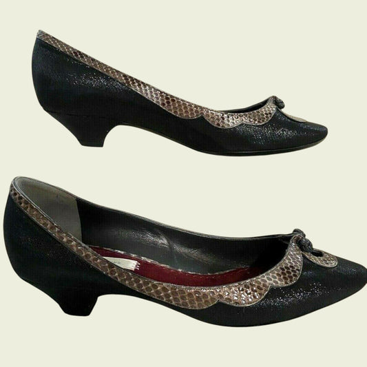 Black high-heeled shoes with decorative brown trim on a beige background