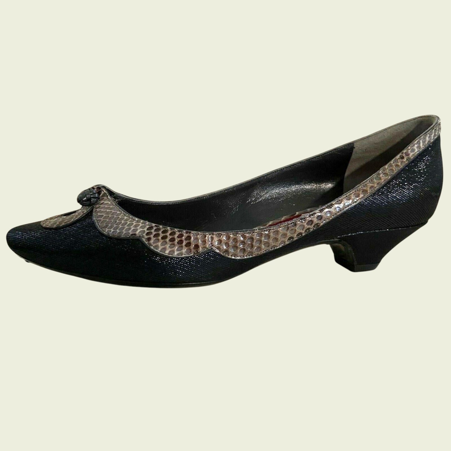 Black shoe with snake print trim on a beige background