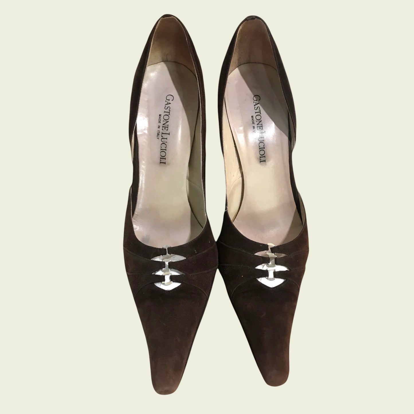 Pair of brown high-heeled shoes with visible brand name on a light beige background
