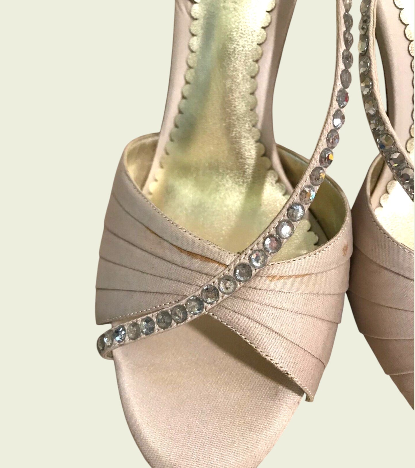 Beige high-heeled shoes with crystal embellishments on a light beige background