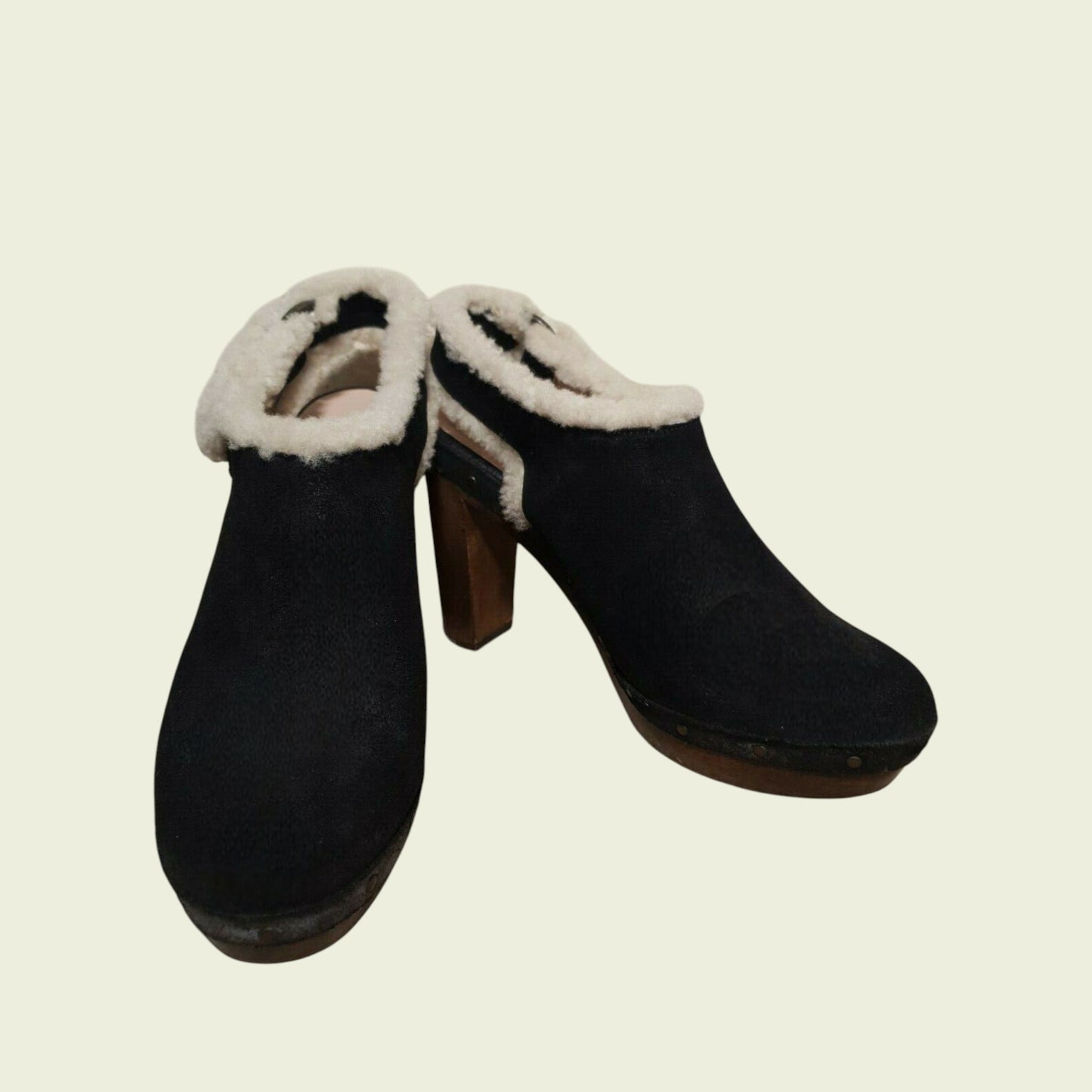 Pair of black clogs with white fur lining on a beige background