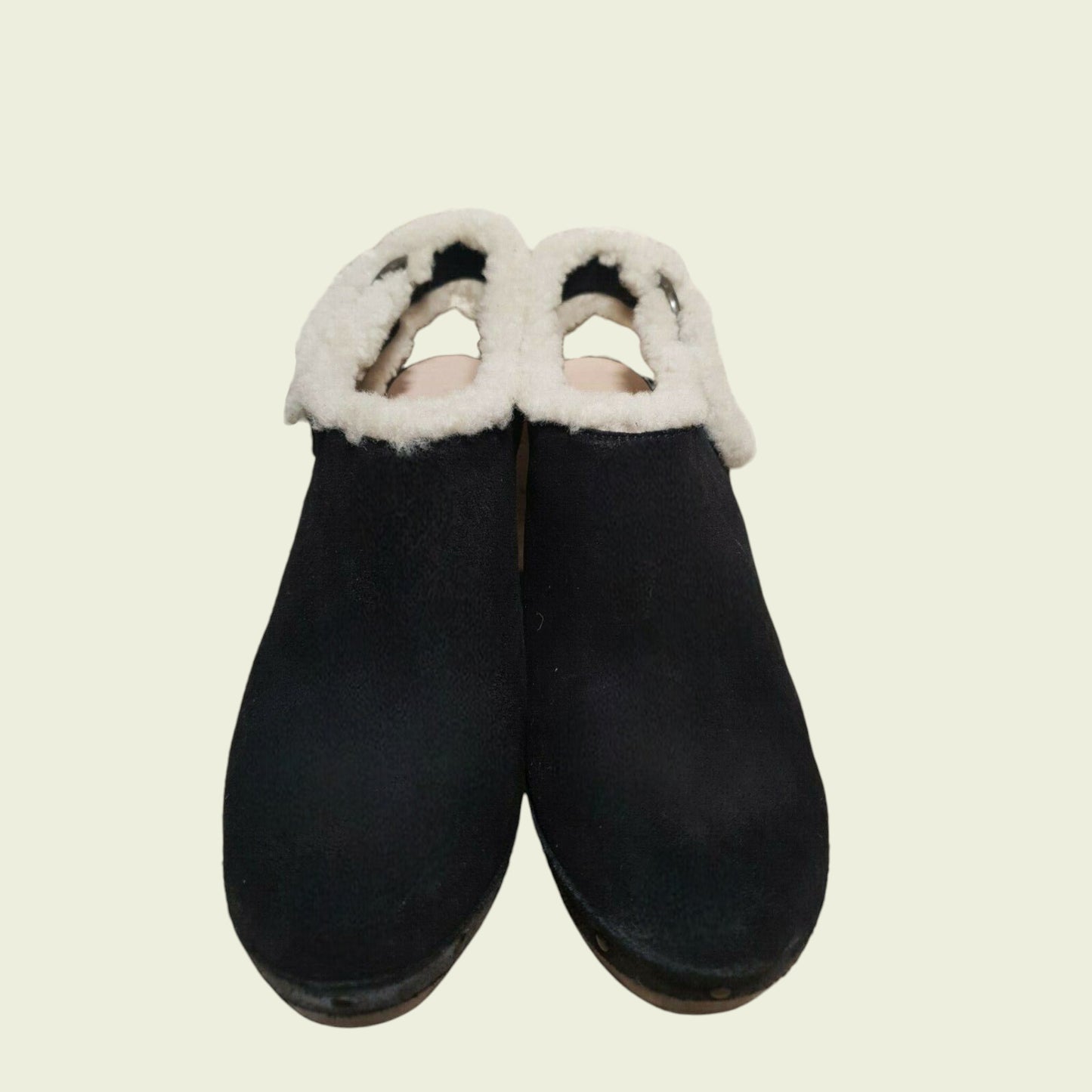 Pair of black clogs with white fur trim on a beige background