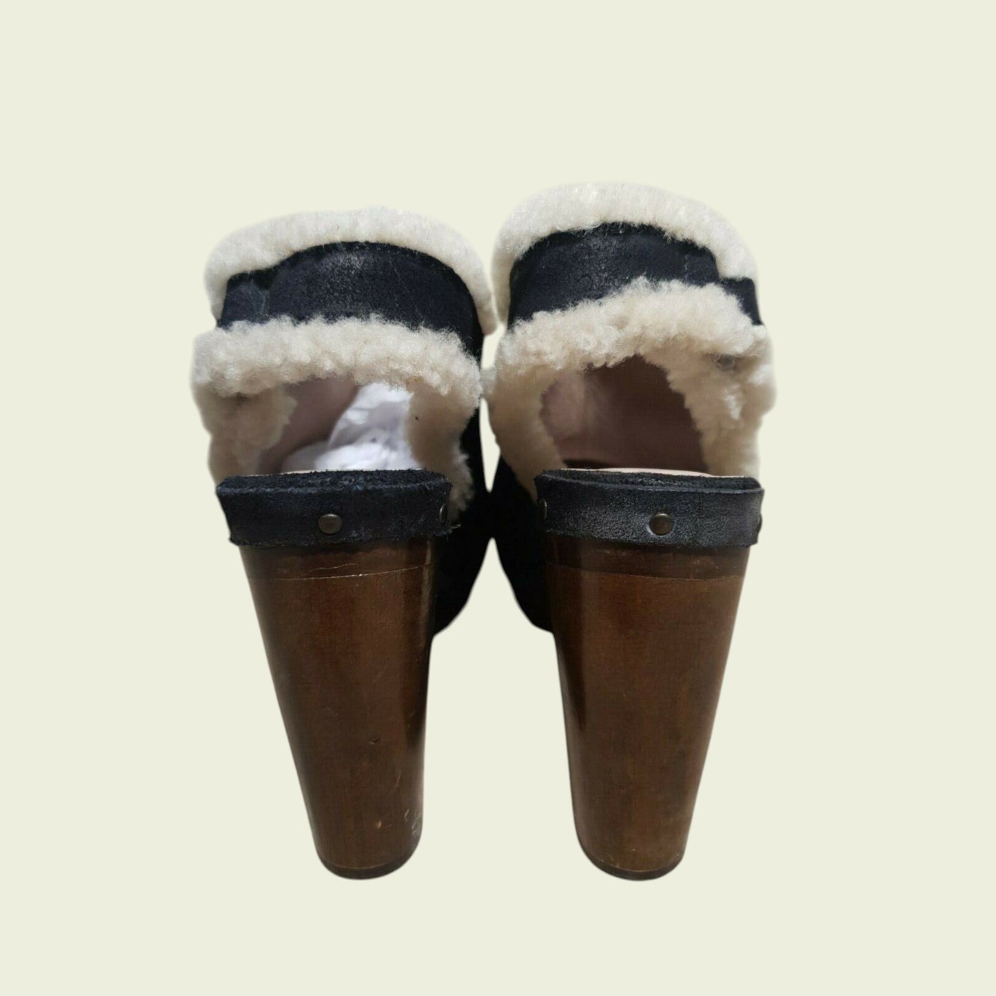 Pair of black mules with white fur lining on a beige background