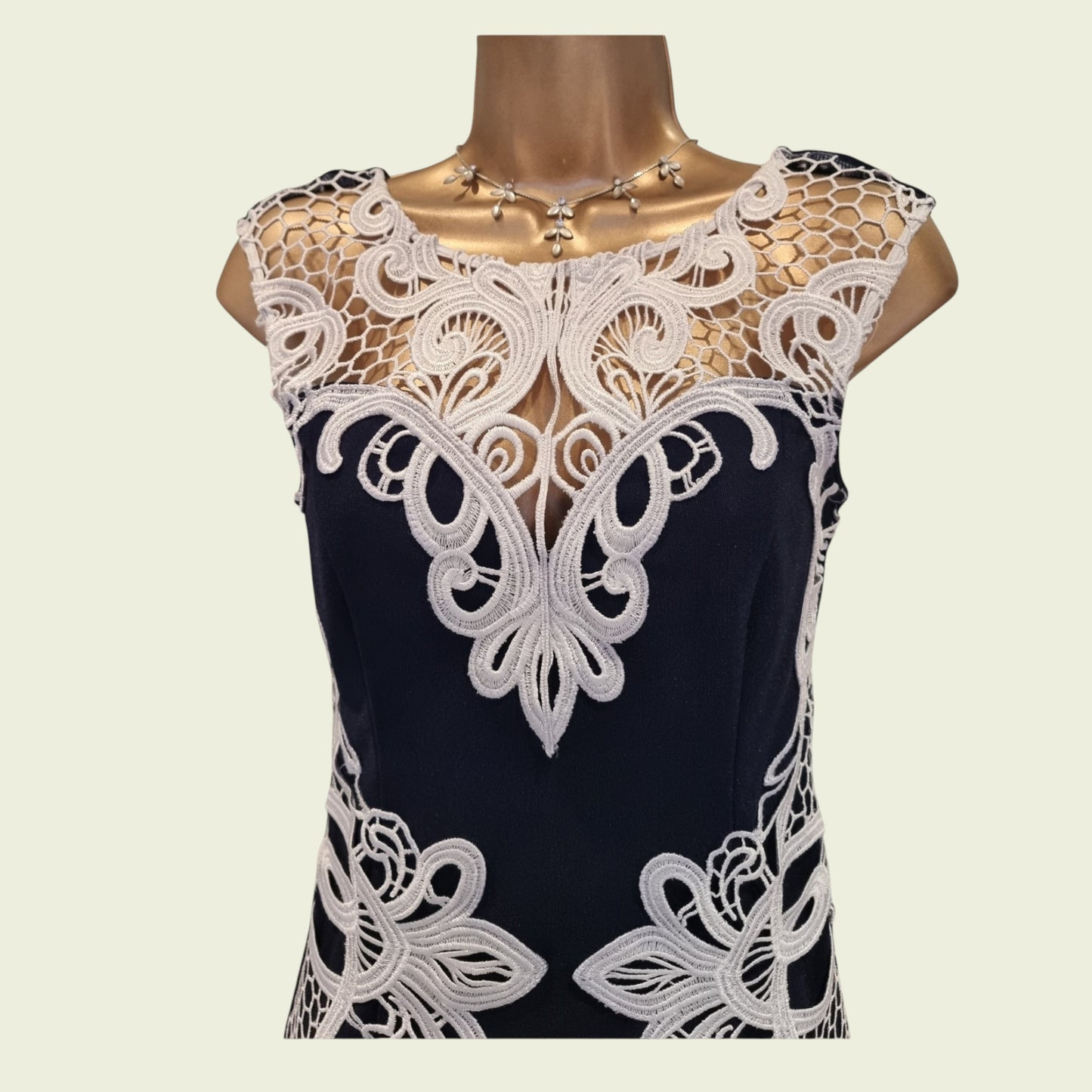 Navy dress with white lace detailing on a mannequin against a beige background