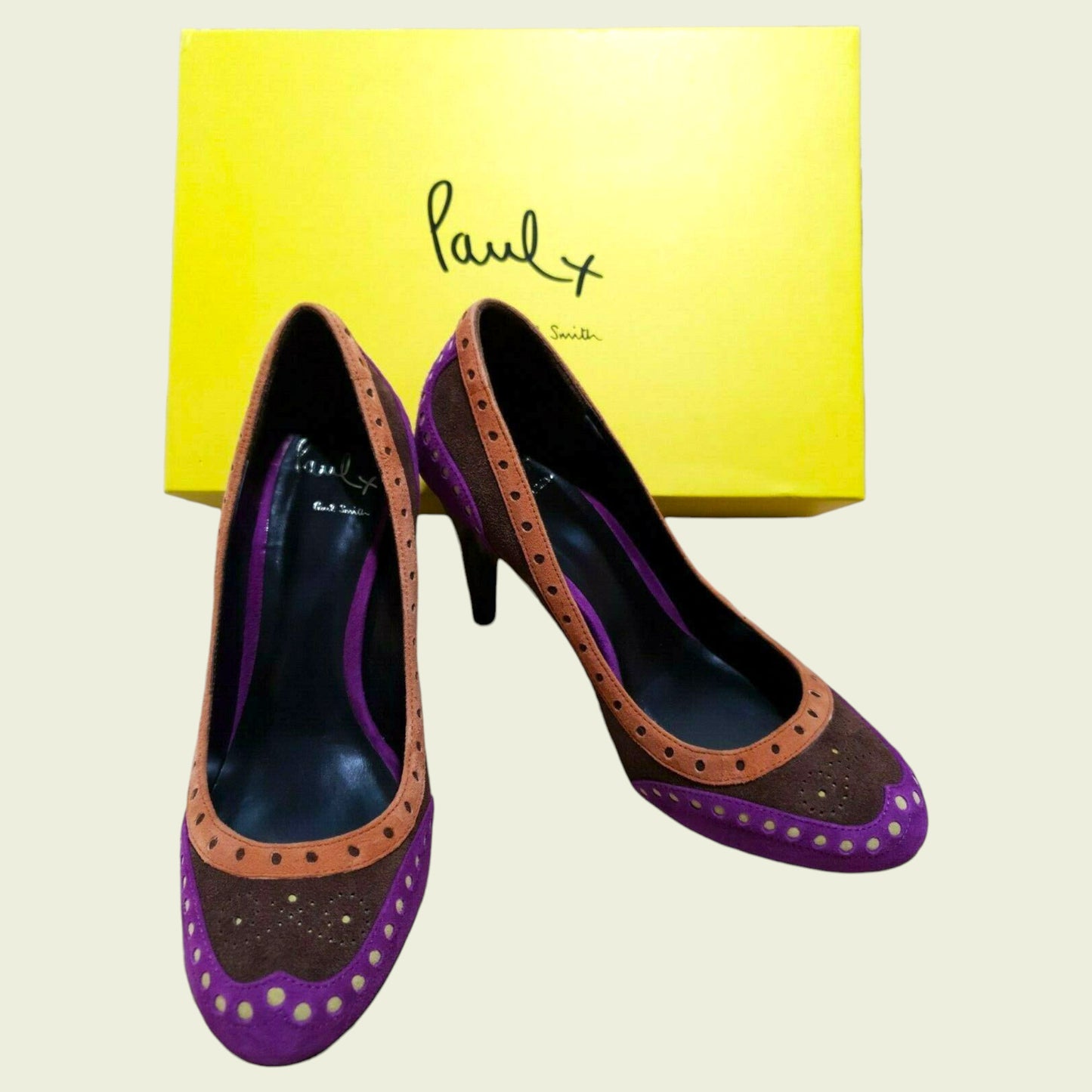 Purple and brown high-heeled shoes with a yellow box featuring 'Paul' branding on a light beige background.