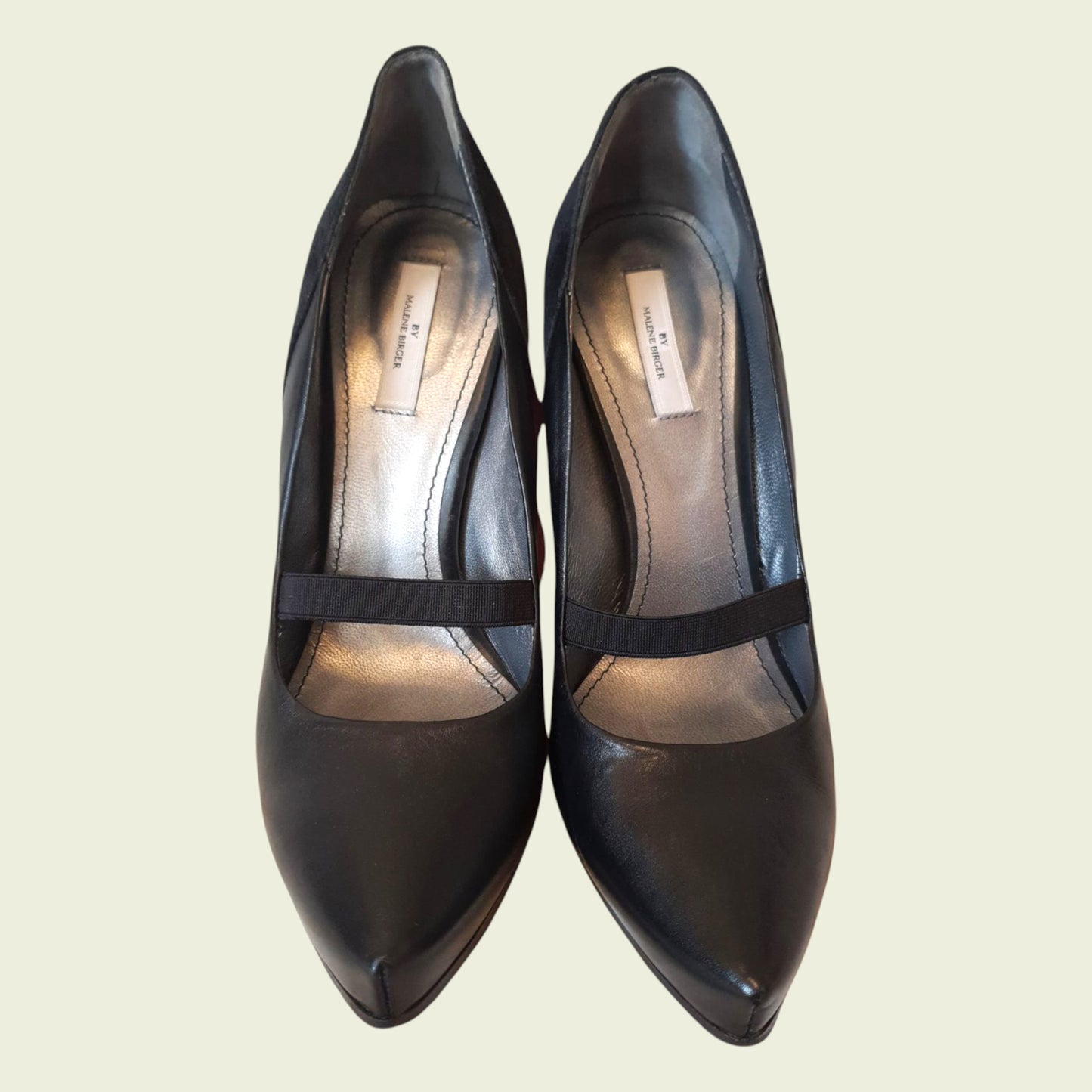 Pair of black high-heeled shoes with a strap on a light beige background