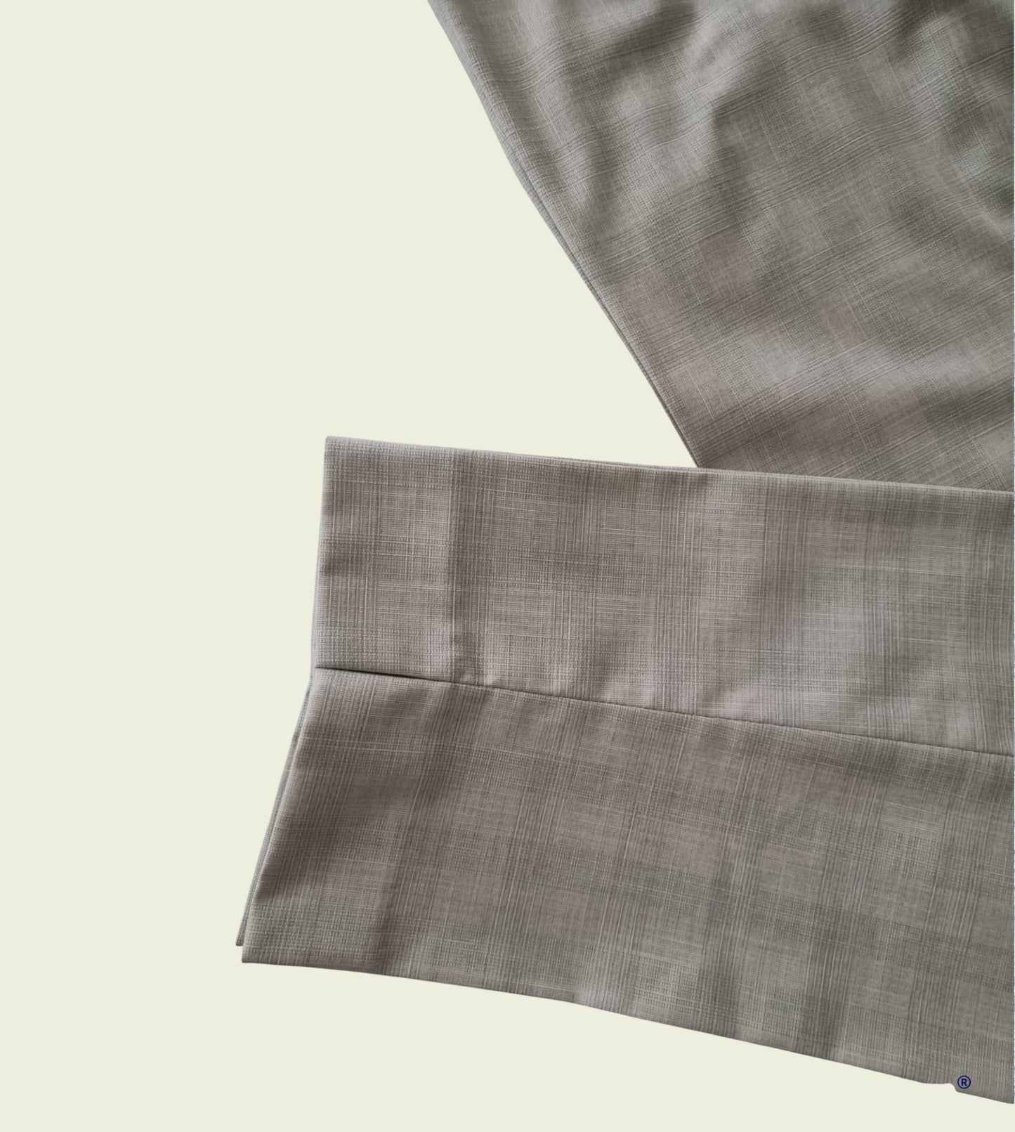 Close-up of mint green trousers with a subtle pattern on a beige background