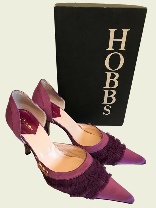 Purple high-heeled shoes with ruffles in front of a black 'Hobbs' box.