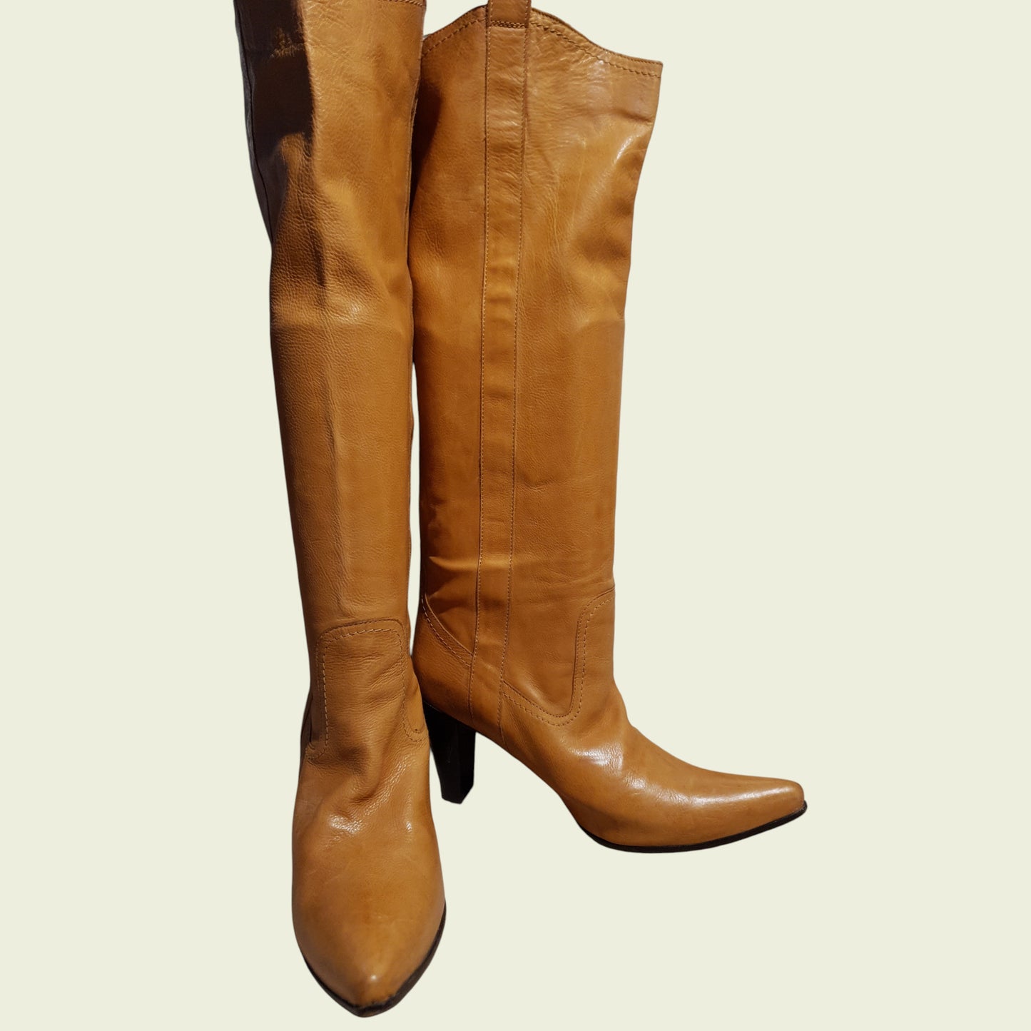 Pair of tan leather knee-high boots on a beige background