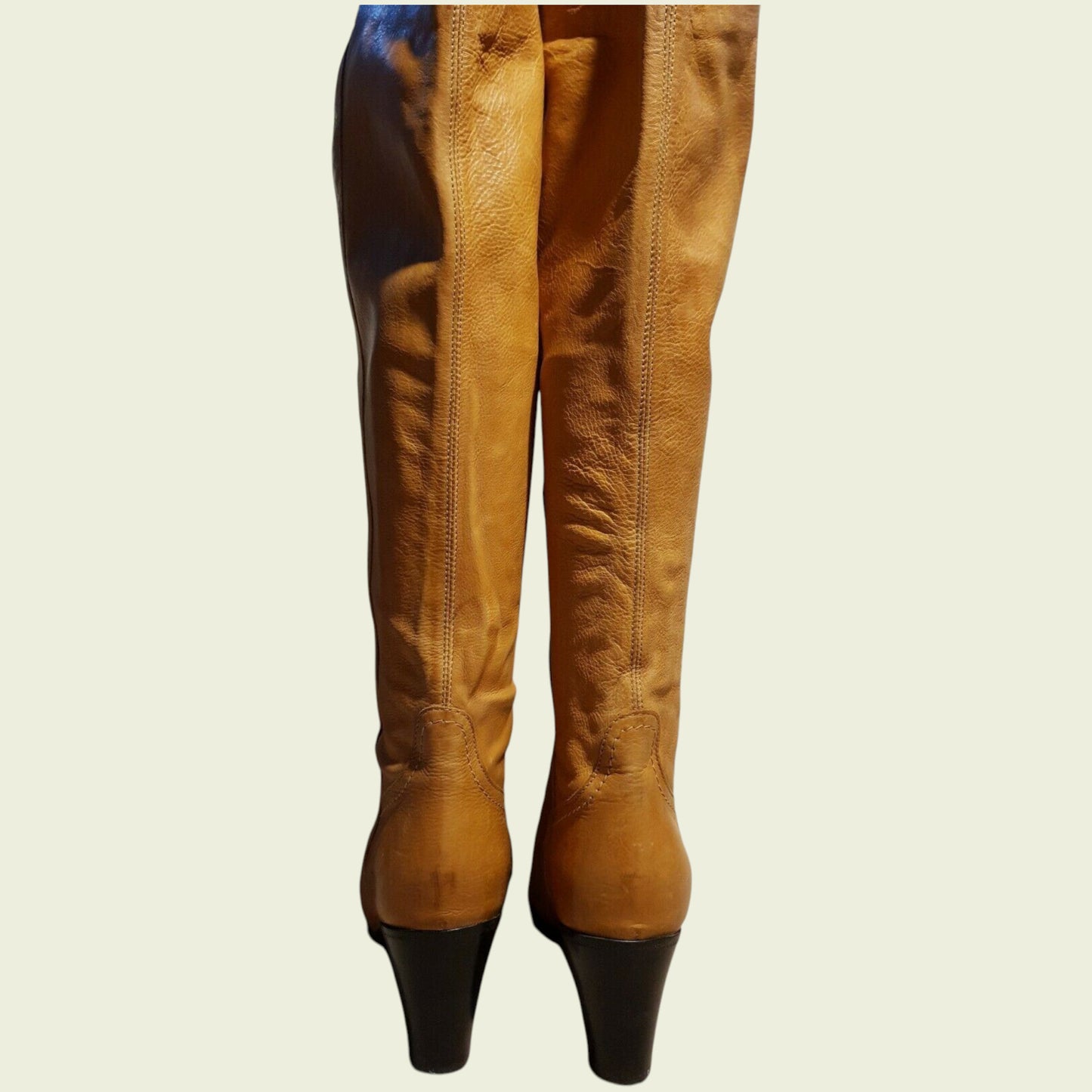 Tan leather boots with black soles on a beige background