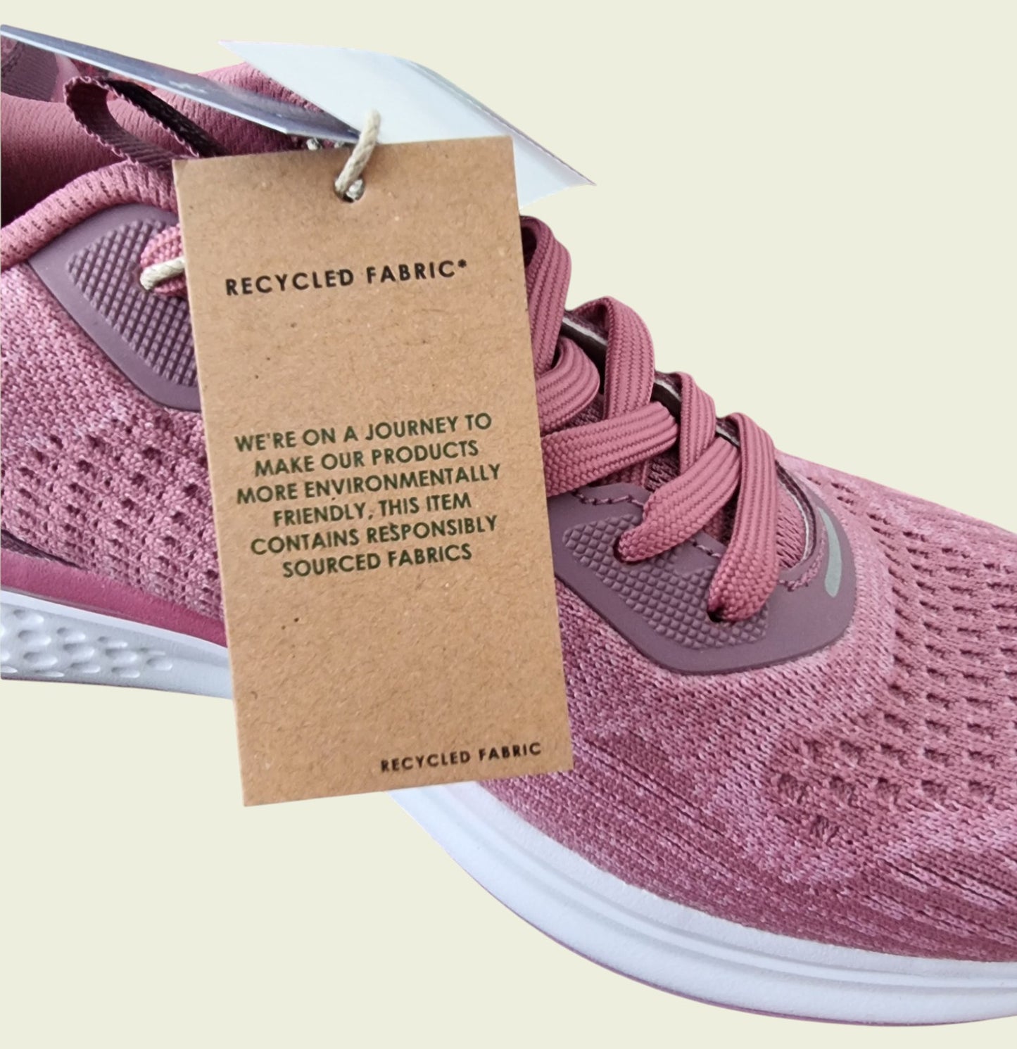 Pink sneaker with a recycled fabric tag on a light beige background