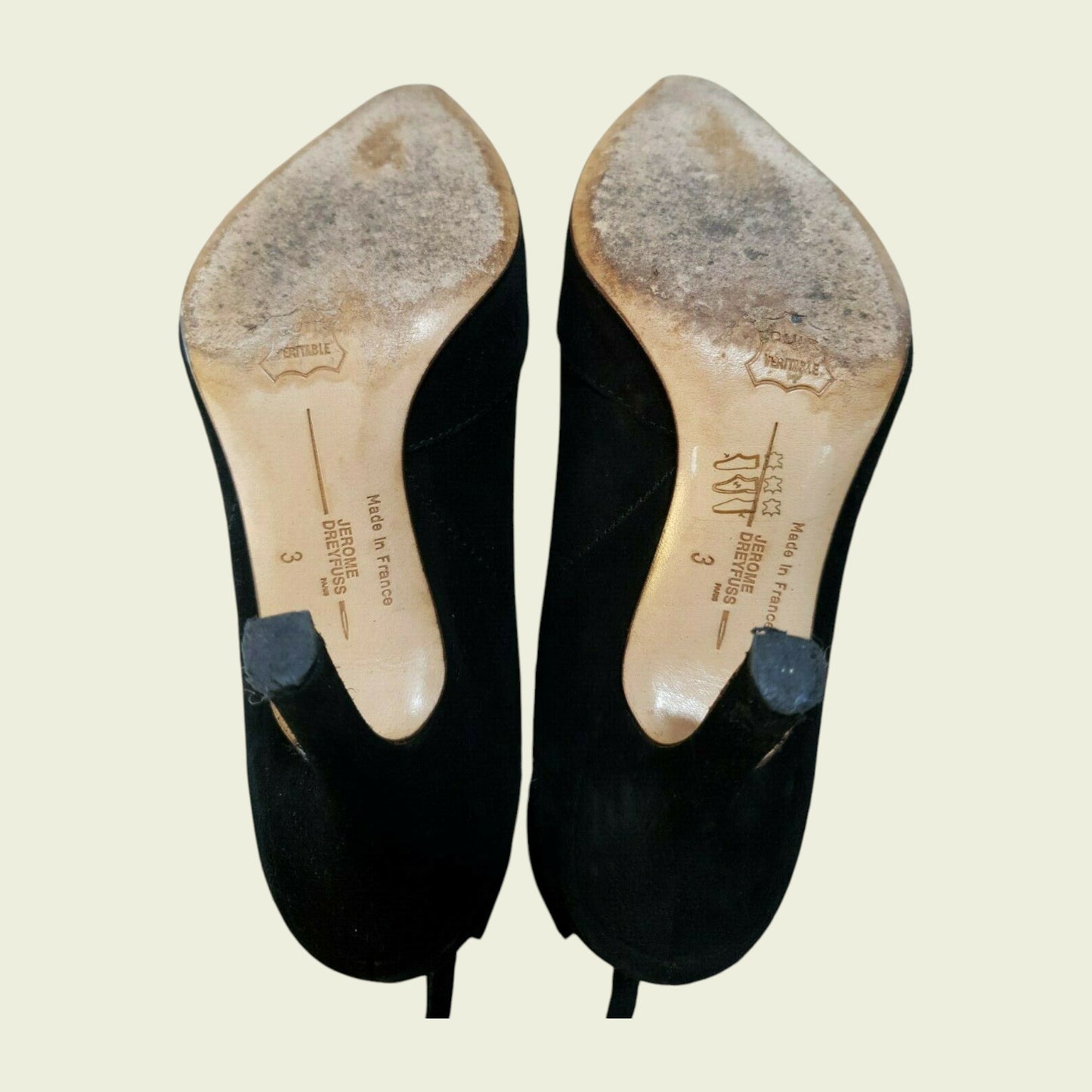Pair of black high-heeled shoes with visible wear on a beige background