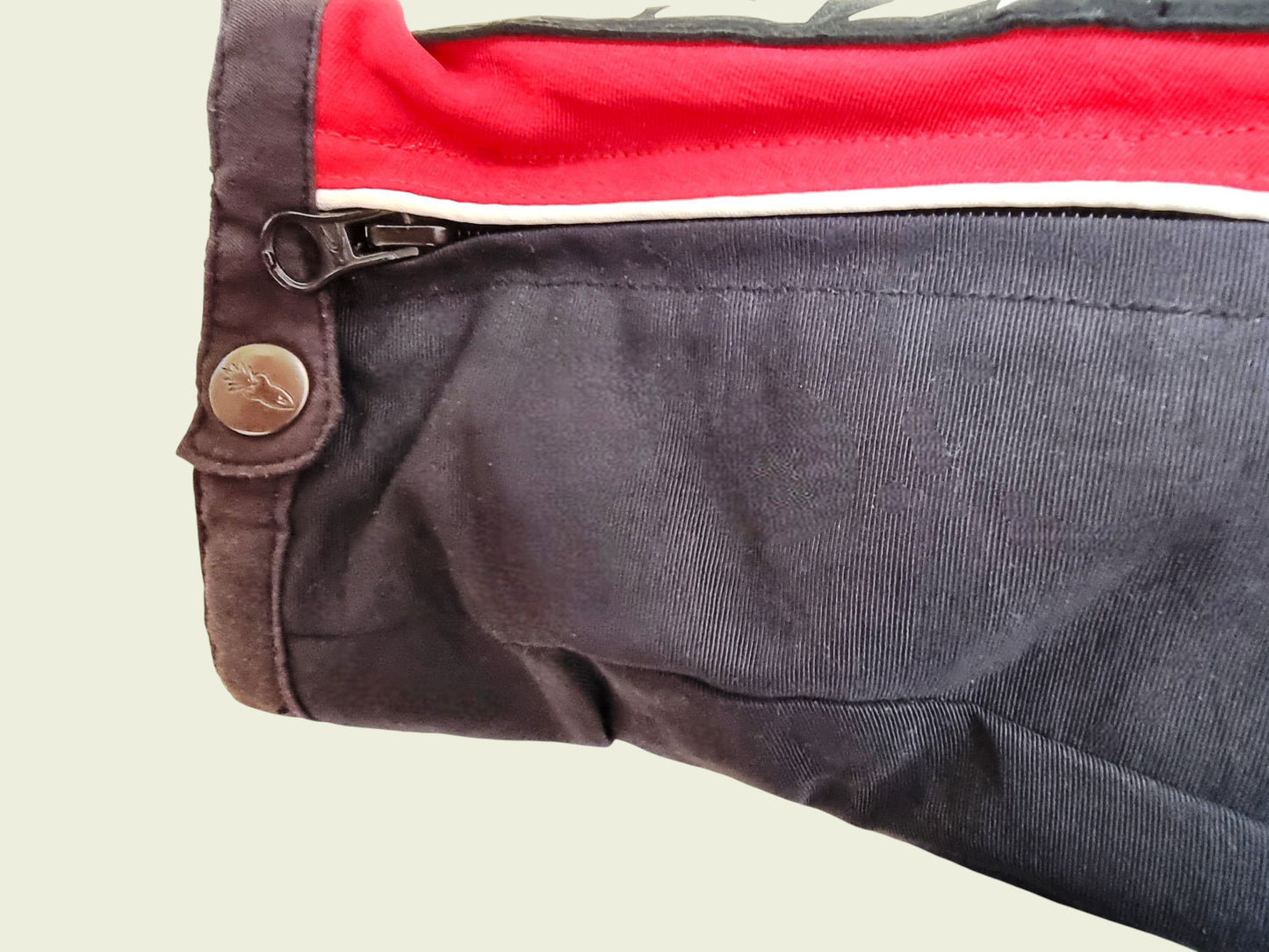 Close-up of a red and black motor cycle jacket with a button on a beige background