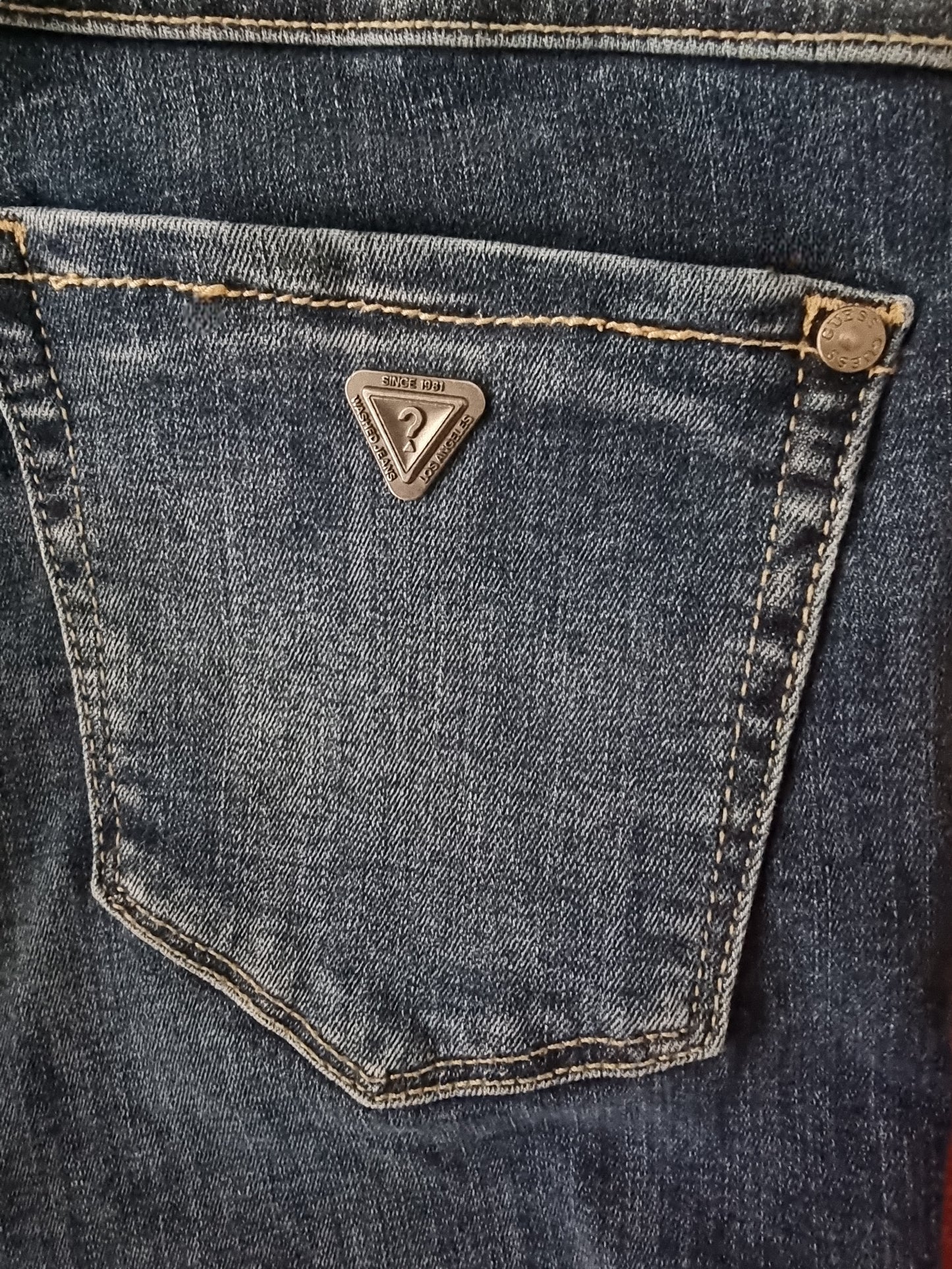 Close-up of a blue denim pocket with a brand logo on a dark background