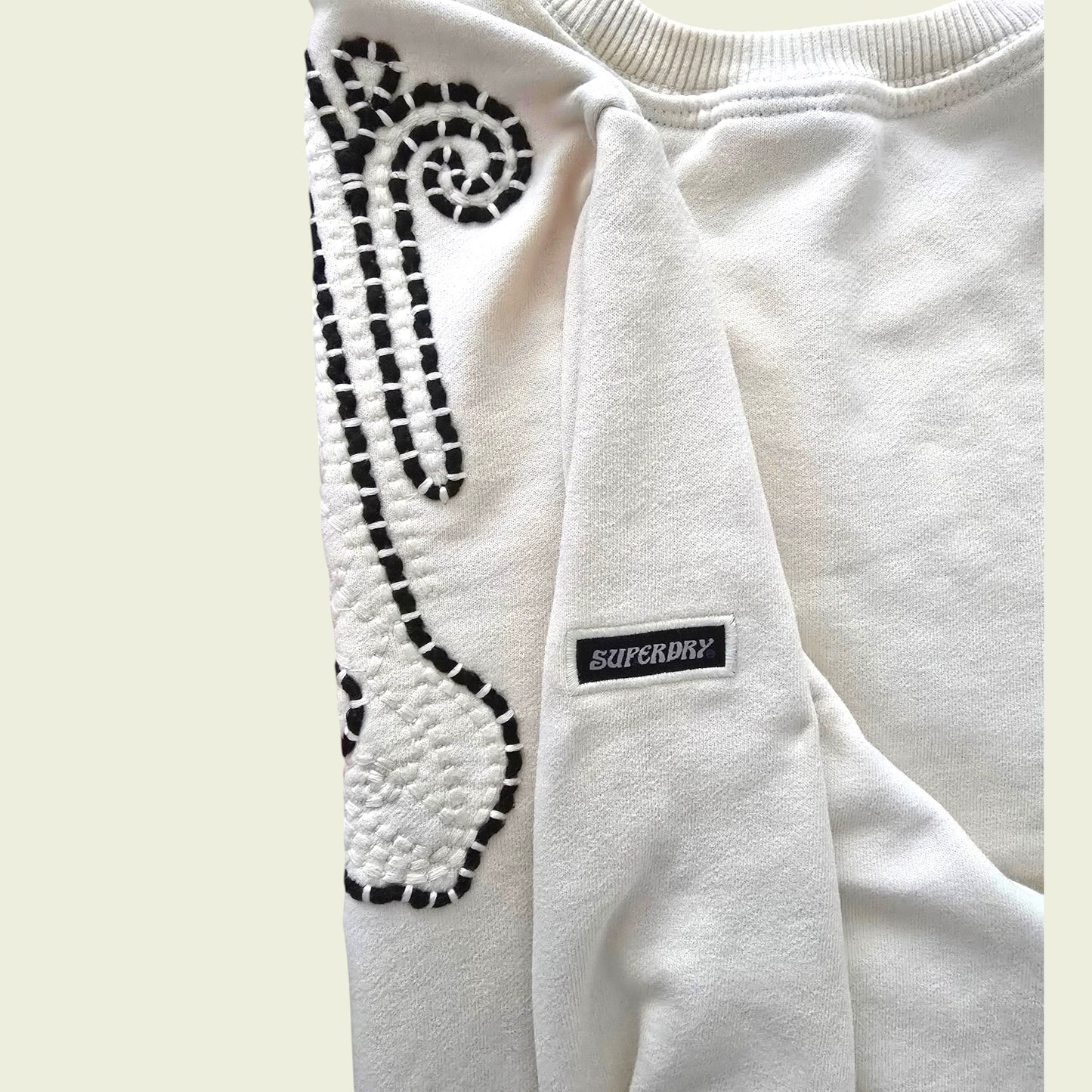 Beige sweatshirt with brown pattern and Superdry logo on a light beige background
