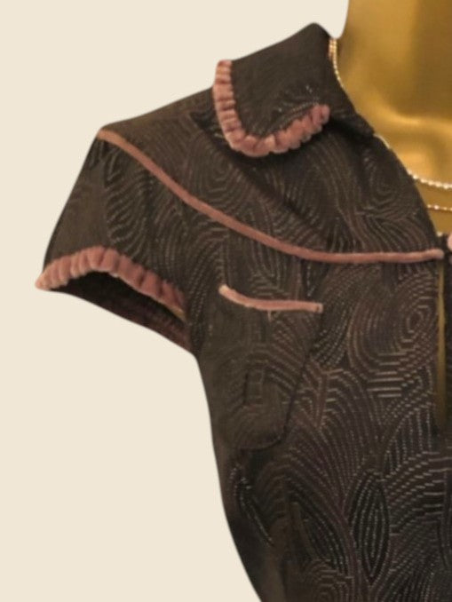 Close-up of a dark fabric garment with intricate patterns and pink trim on a beige background