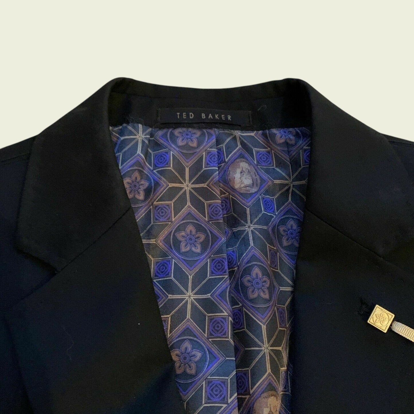 Black suit jacket with a patterned tie and Ted Baker label on a beige background