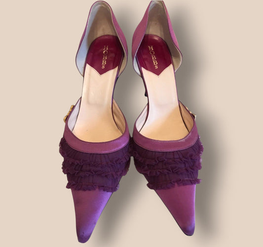 Purple high-heeled shoes with ruffled details on a beige background