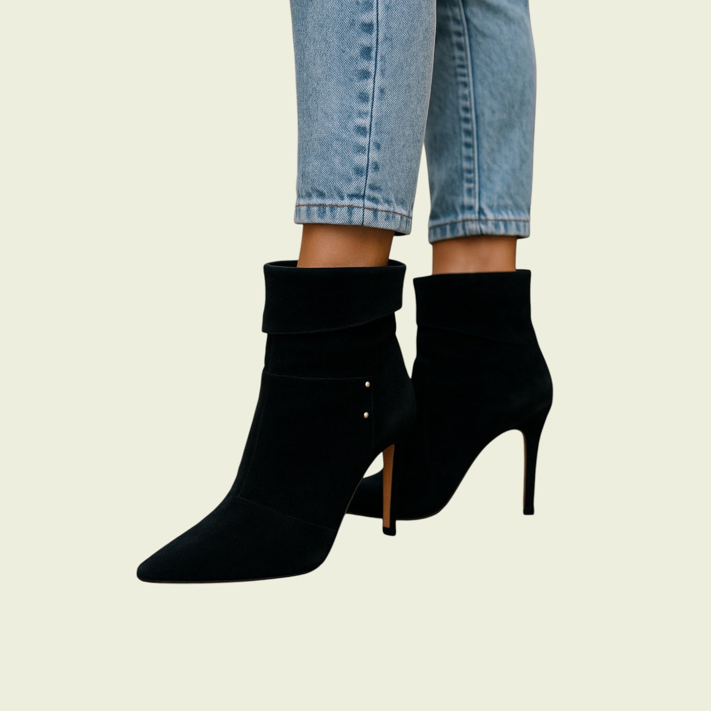 Black high-heeled ankle boots worn with light blue jeans on a beige background