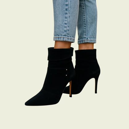 Black high-heeled ankle boots worn with light blue jeans on a beige background