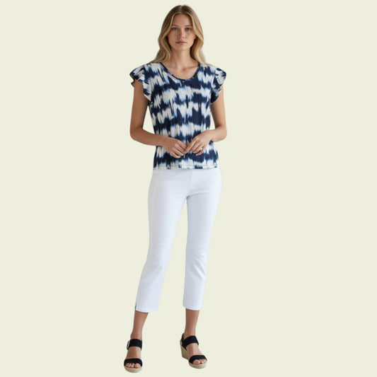 Woman wearing a blue and white patterned top with white pants on a beige background