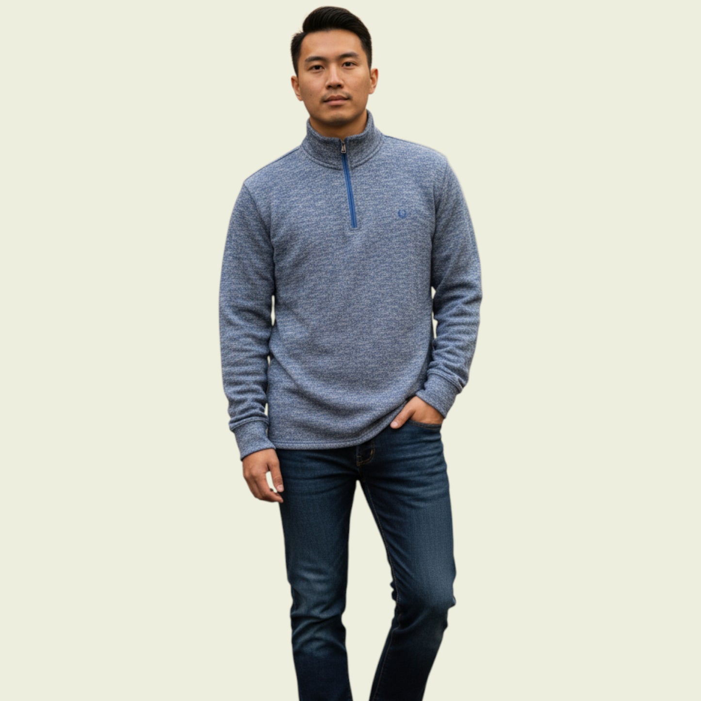 Man wearing a blue half-zip sweater and dark jeans on a beige background