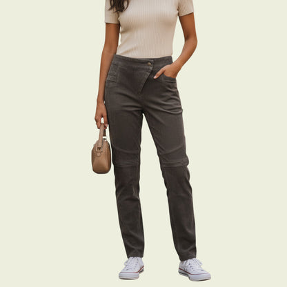 Person wearing dark gray pants and a beige top, standing against a light beige background