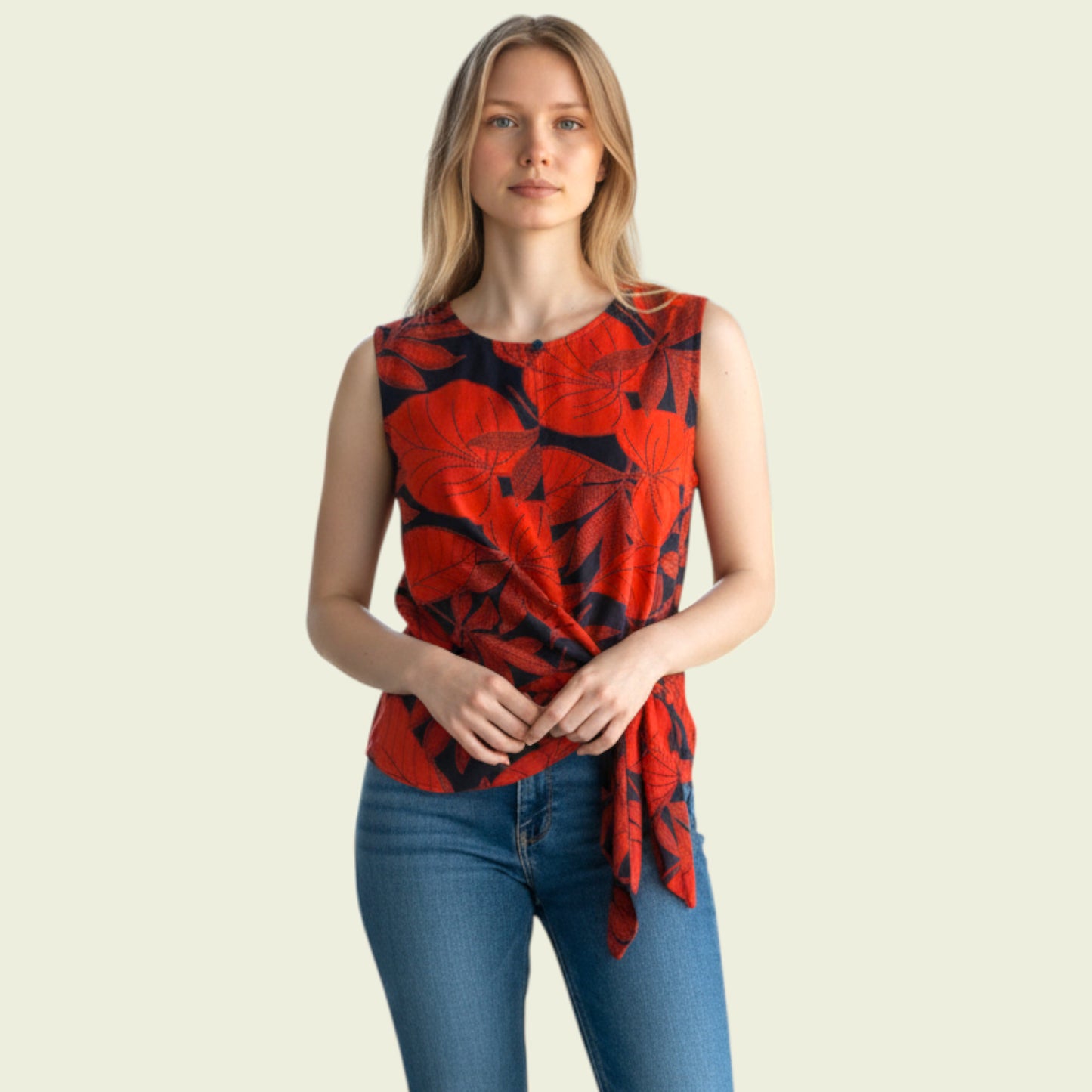 Woman wearing a red and black patterned sleeveless top with blue jeans on a beige background