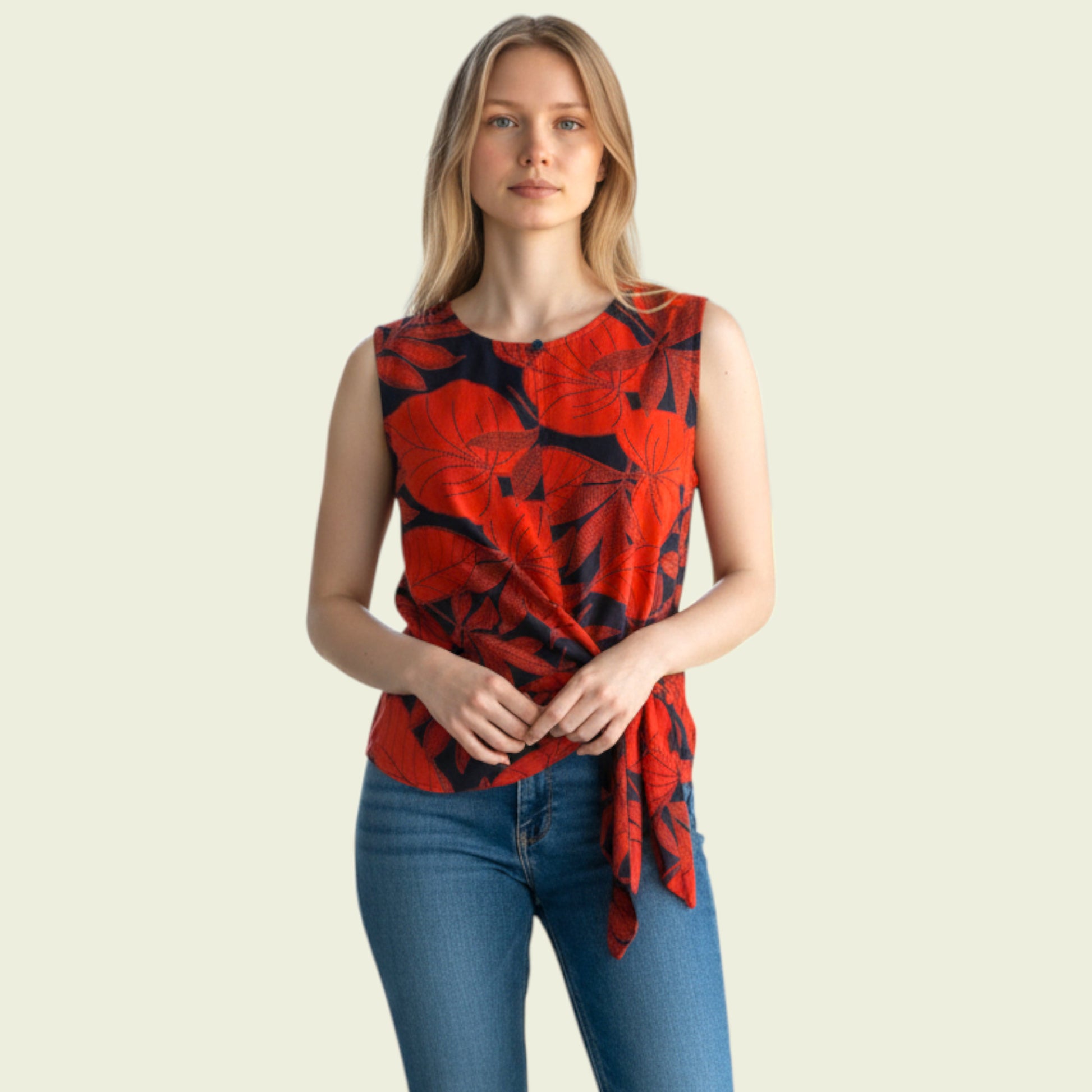 Woman wearing a red and black patterned sleeveless top with blue jeans on a beige background