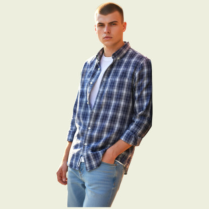Man wearing a blue plaid shirt over a white t-shirt with light blue jeans on a beige background