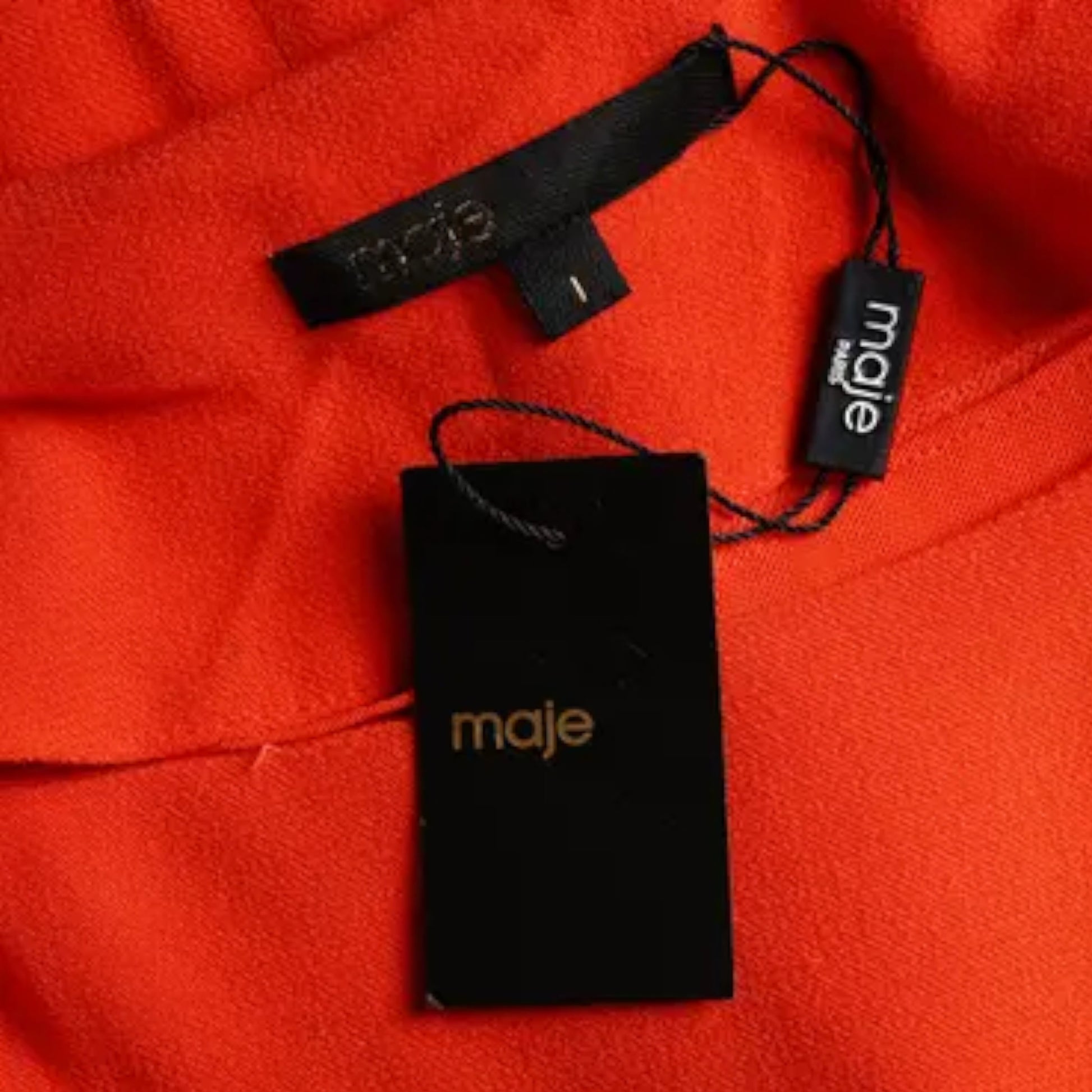 Maje branded tag on a red fabric background
