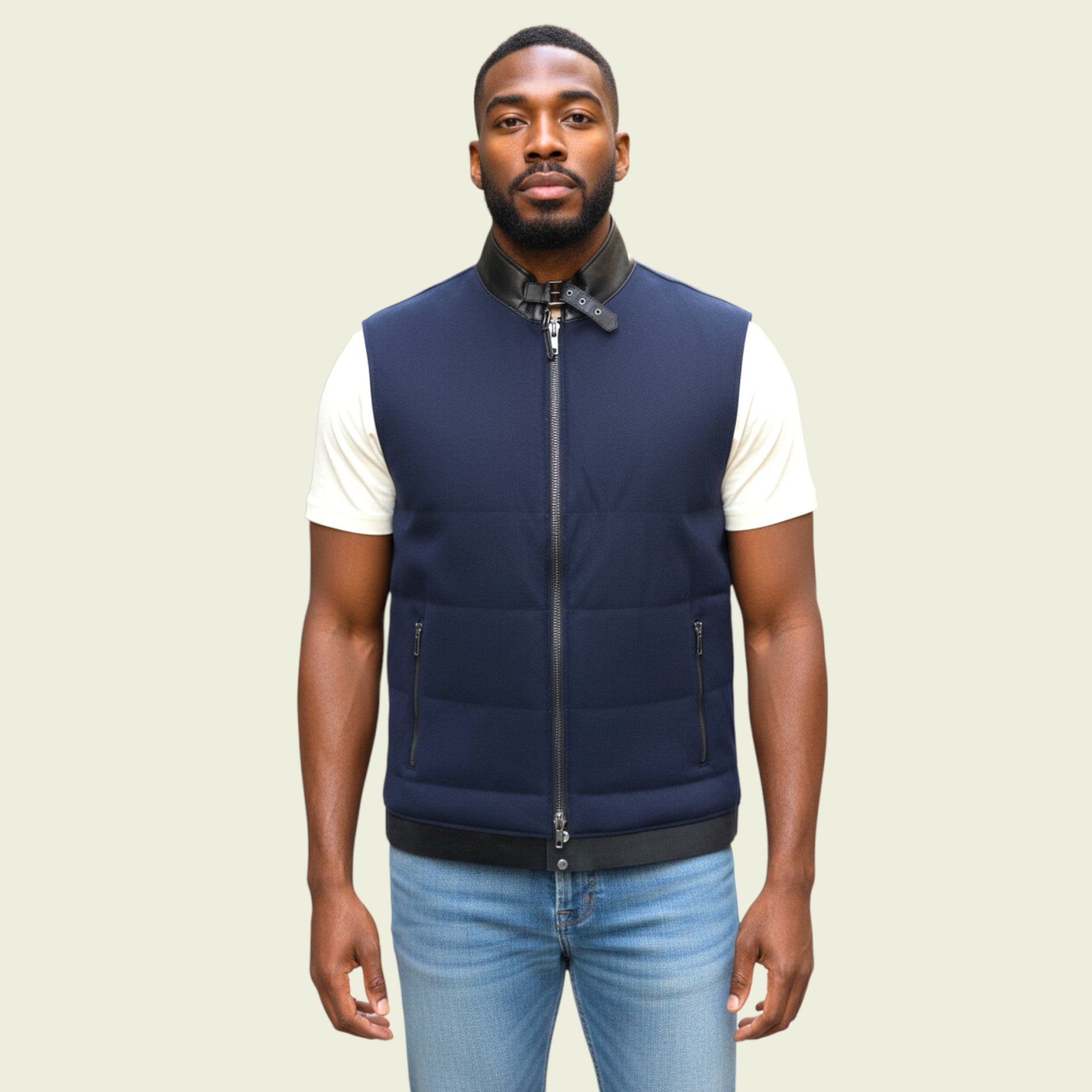 Man wearing a navy blue vest over a white shirt with light blue jeans on a beige background