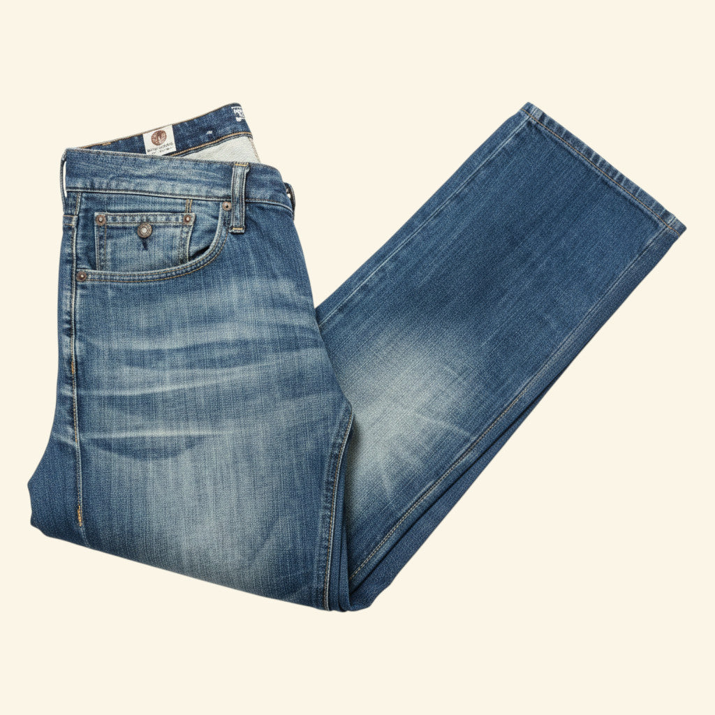 A pair of medium-wash blue denim jeans folded diagonally on a solid cream-colored background.
