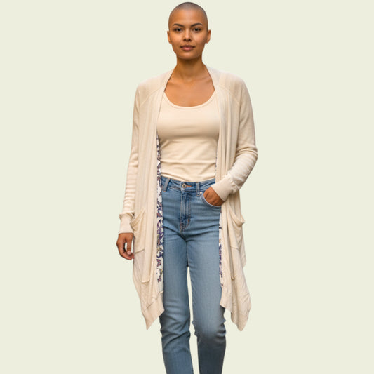 Woman wearing a beige cardigan, white top, and blue jeans on a light green background