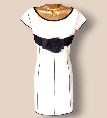 White dress with black belt and flower detail on a beige background