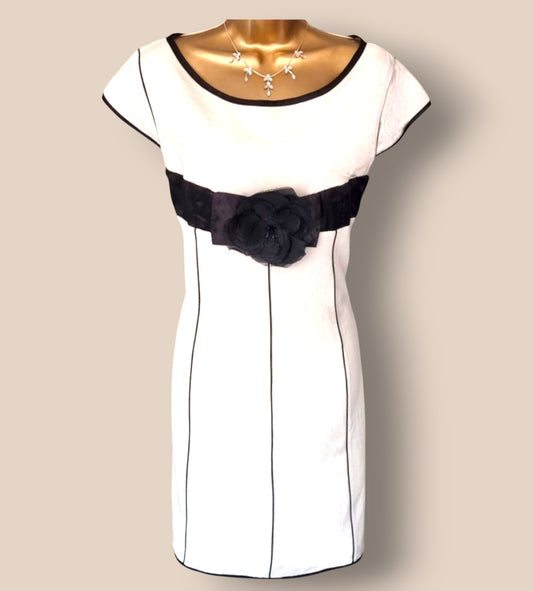 White dress with black belt and flower detail on a beige background