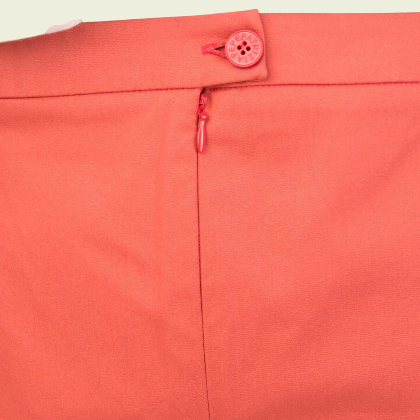 Close-up of a coral-colored garment with a button and zipper detail on a beige background