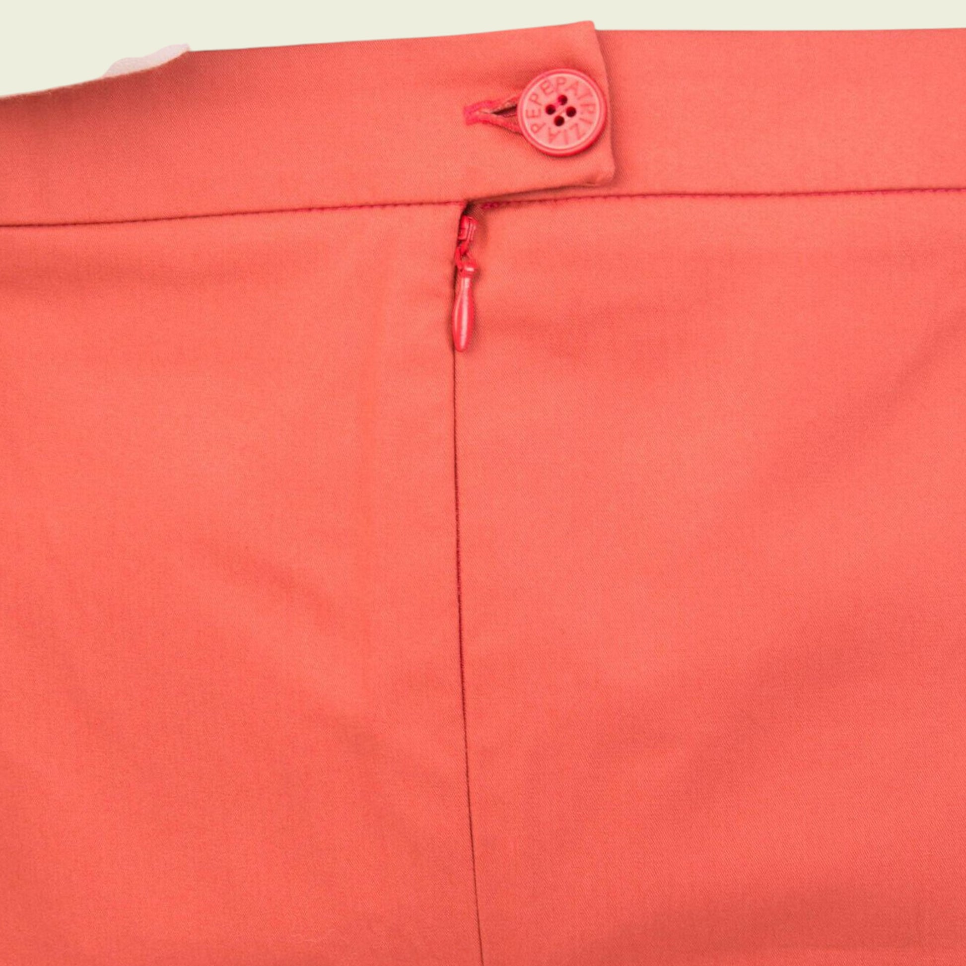 Close-up of a coral-colored garment with a button and zipper detail on a beige background