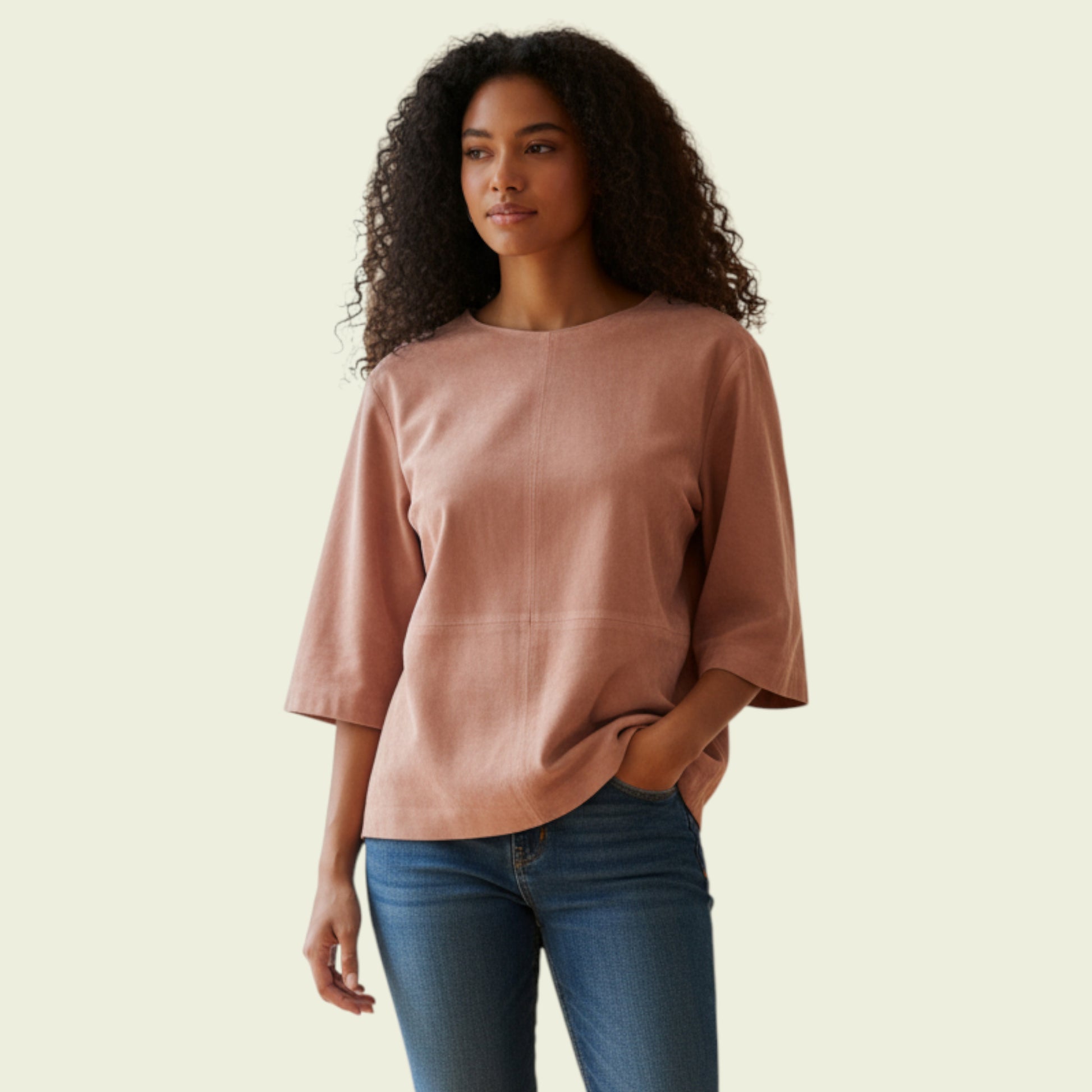 Woman wearing a tan top and blue jeans against a beige background