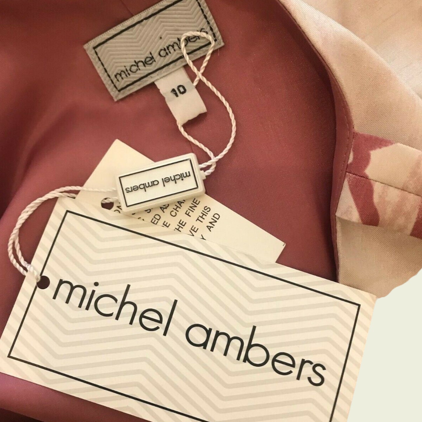 Dress label with MICHEL AMBERS and size details on pink background