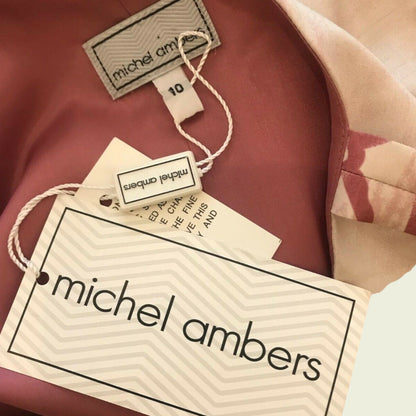 Dress label with MICHEL AMBERS and size details on pink background