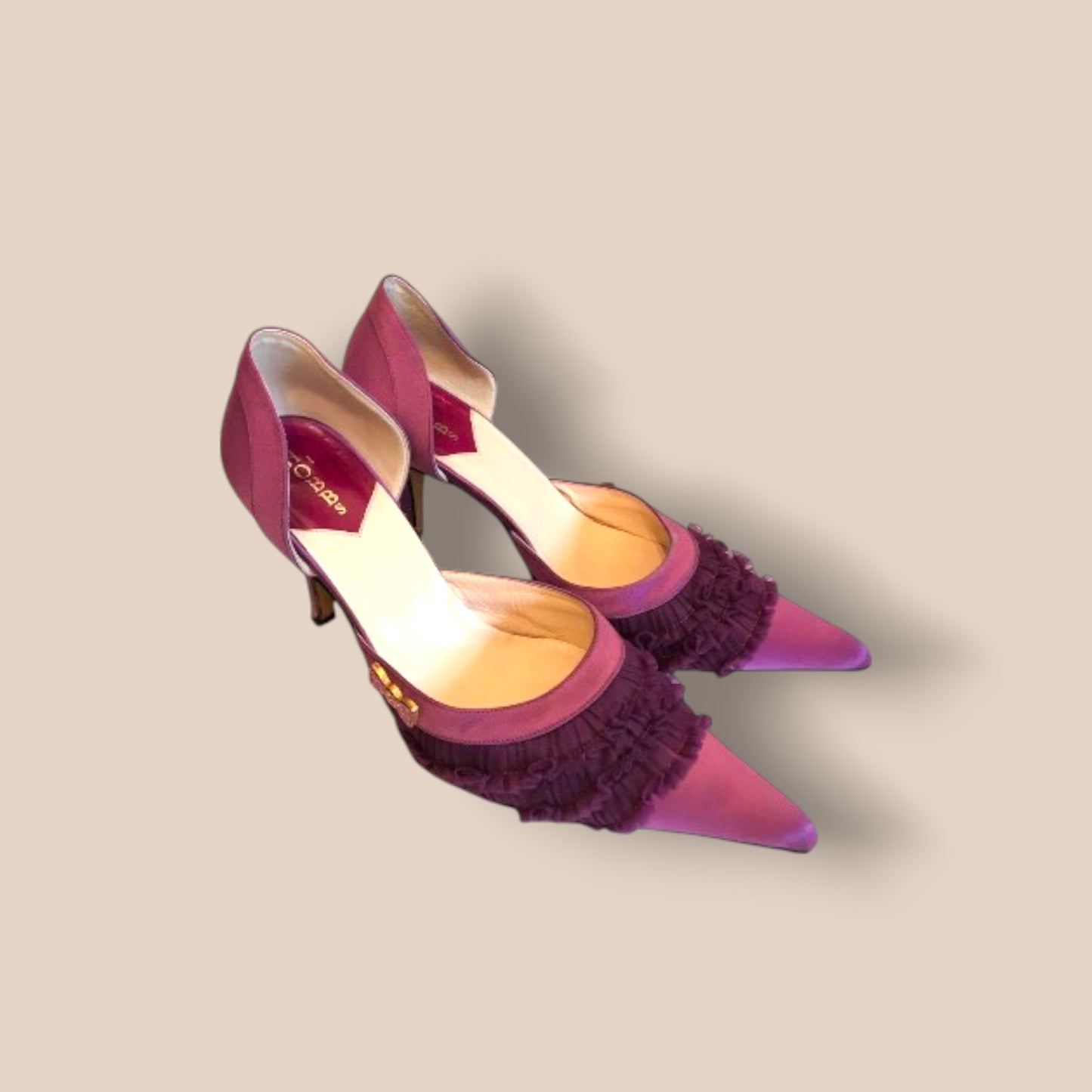Pair of purple high-heeled shoes with ruffled details on a beige background