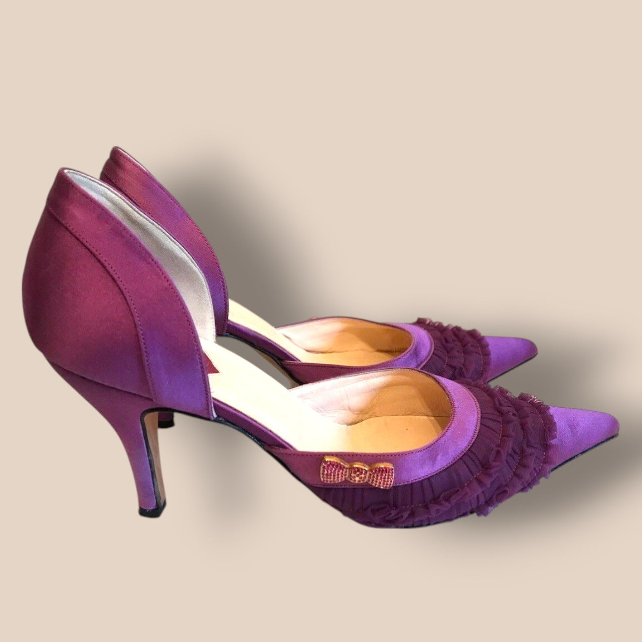 Purple high-heeled shoes with ruffled details on a beige background