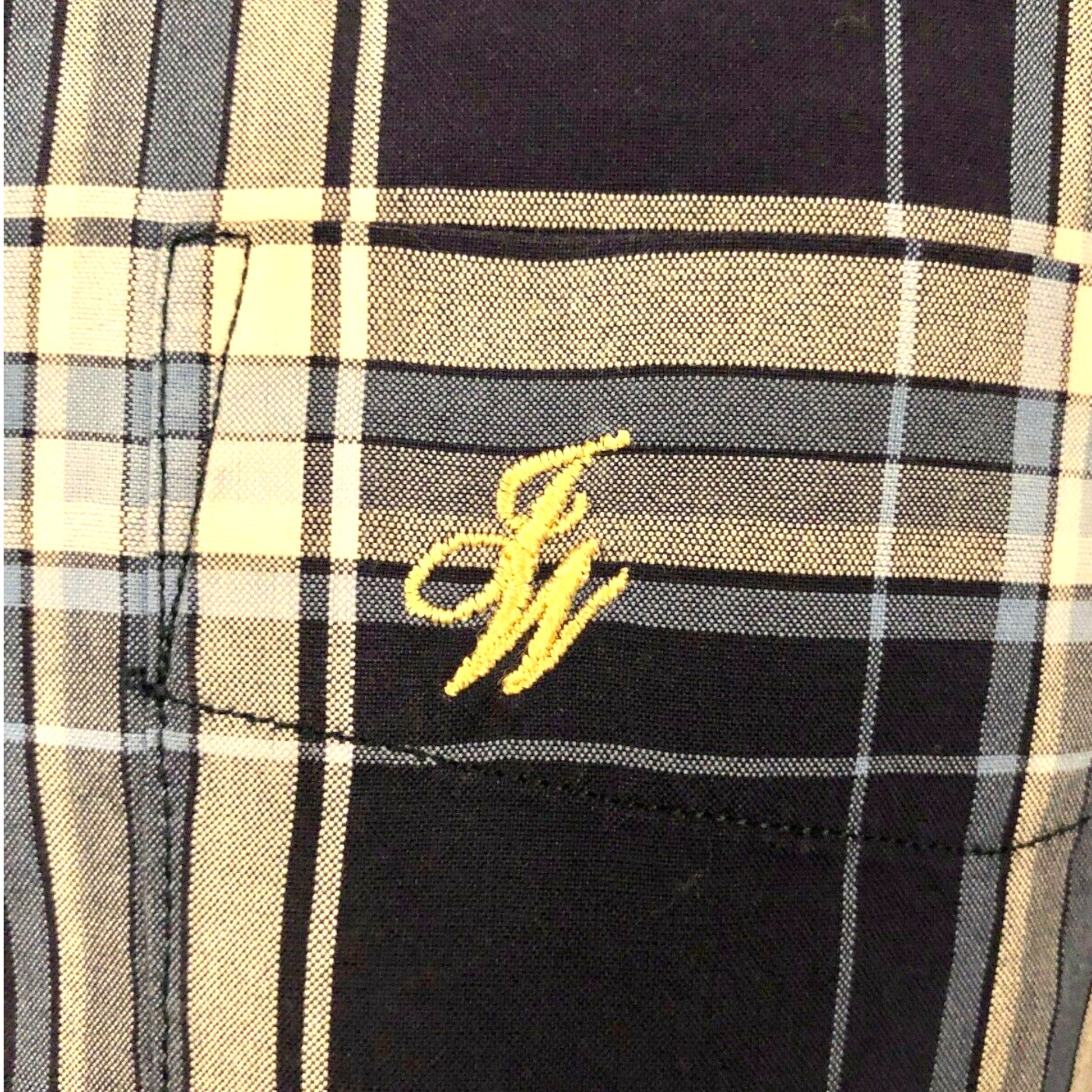 Plaid shirt pocket with yellow embroidered logo on a black and beige checkered fabric.