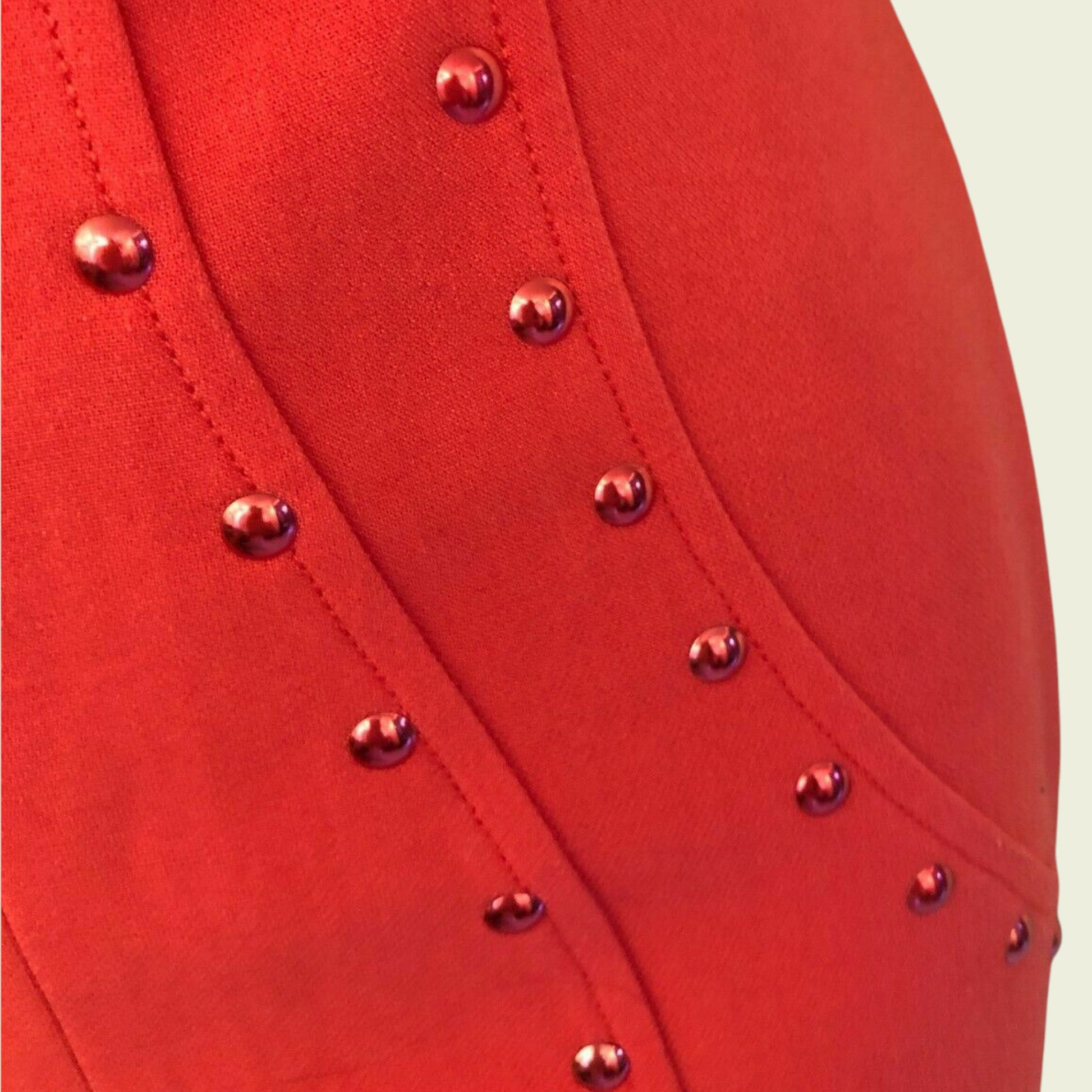 Close-up of a red garment with metallic buttons on a beige background
