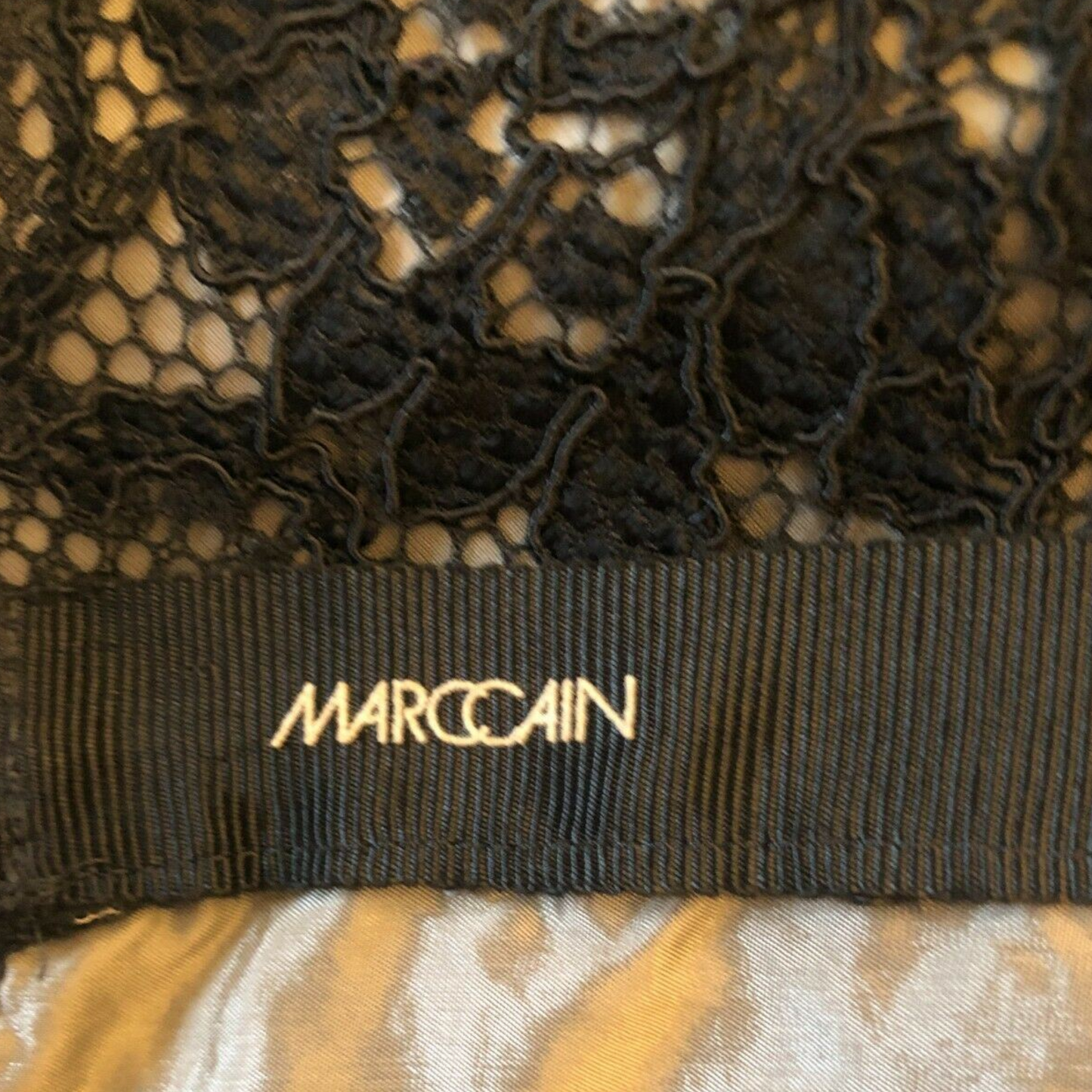 Black lace garment with 'Marc Cain' label on a patterned background