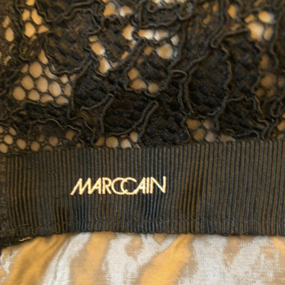 Black lace garment with 'Marc Cain' label on a patterned background