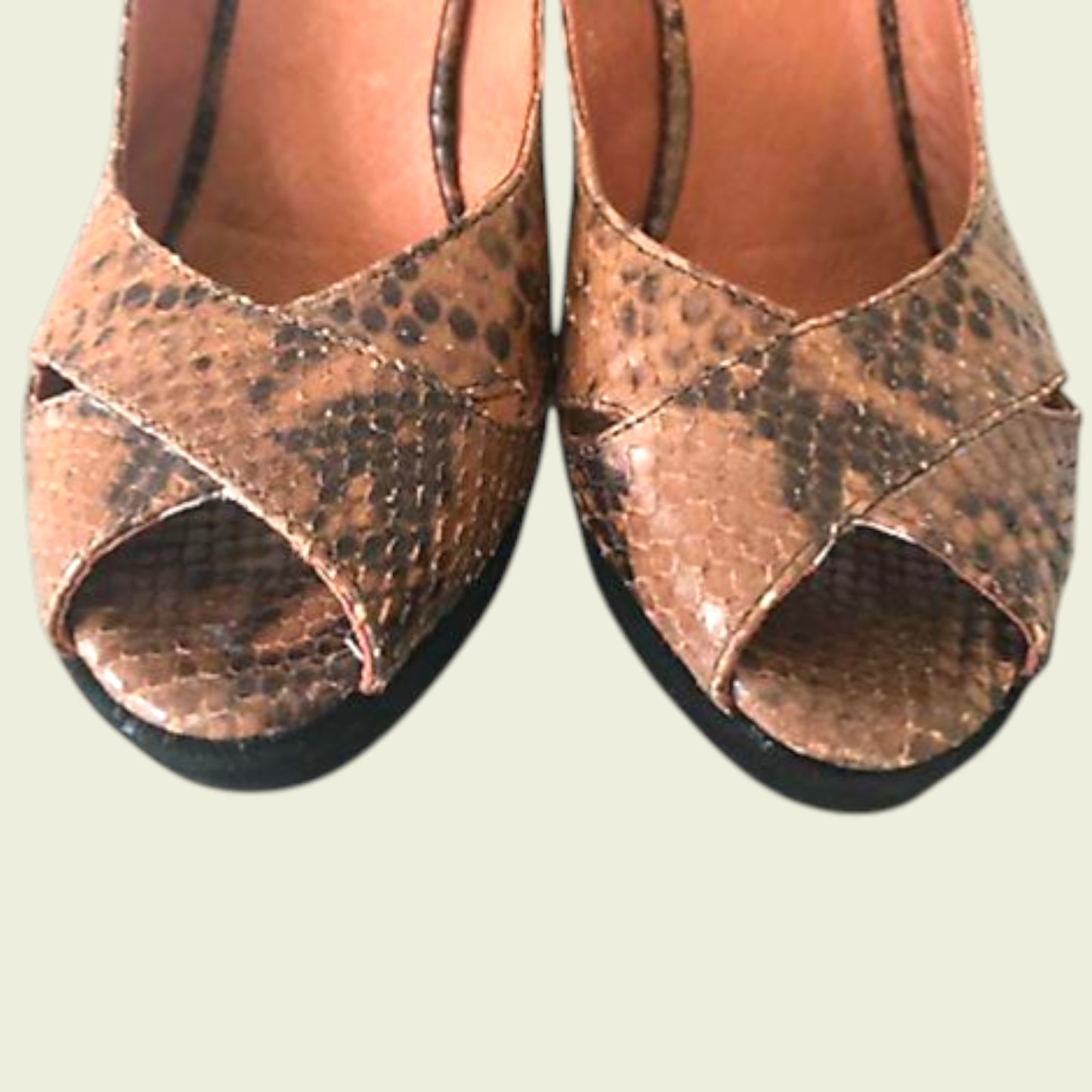 Close up of pair of brown open-toe sandals with snake print on a light background