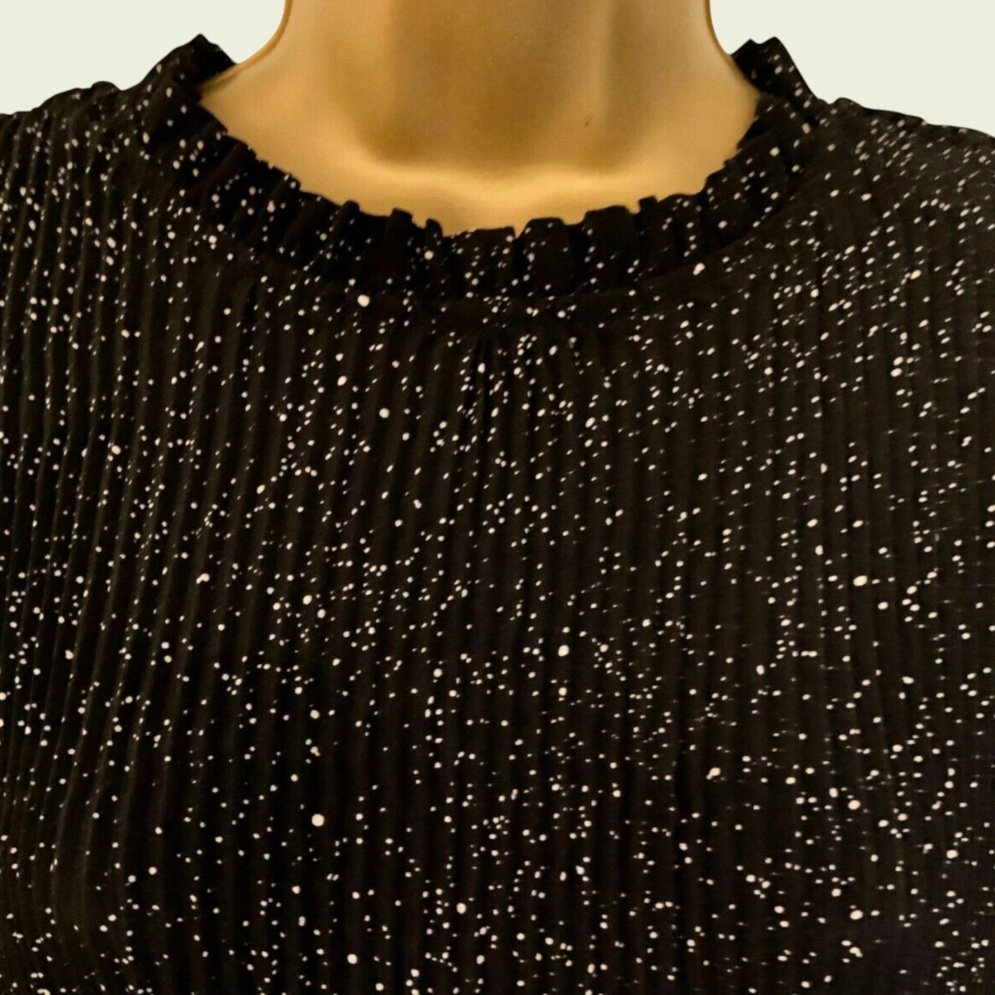 Neckline of black and white polka dot pleated dress on beige background