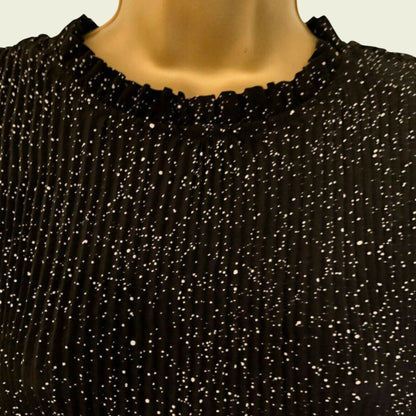 Neckline of black and white polka dot pleated dress on beige background